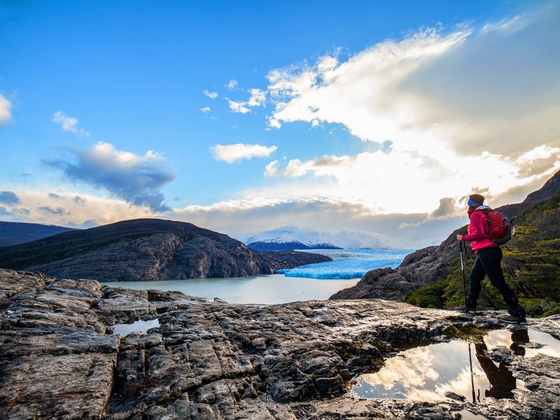 Hiker in red jacket gazes at turquoise Glaciar Grey and surrounding peaks in Torres del Paine, Patagonia.
