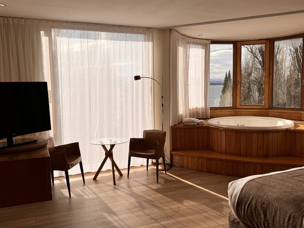 Luxury hotel suite in Bariloche with lake views, spa tub, modern furnishings, and floor-to-ceiling windows overlooking Patagonian landscape.