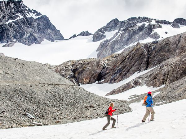 Hikers trekking across snowy terrain with dramatic rocky peaks and Glaciar Vinciguerra in Patagonia.