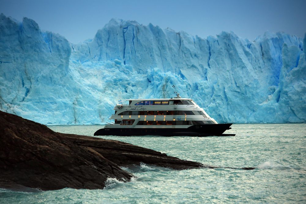 Luxury cruise ship anchored before the towering blue ice walls of Perito Moreno Glacier in Patagonia.