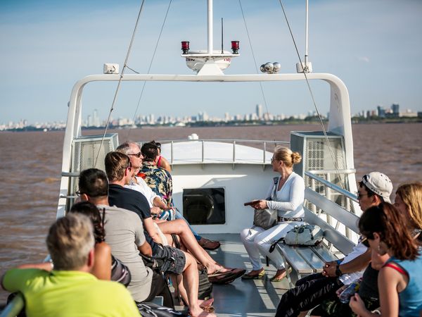 Tourists enjoy a guided boat tour through the Tigre Delta near Buenos Aires with the city skyline visible in the distance.