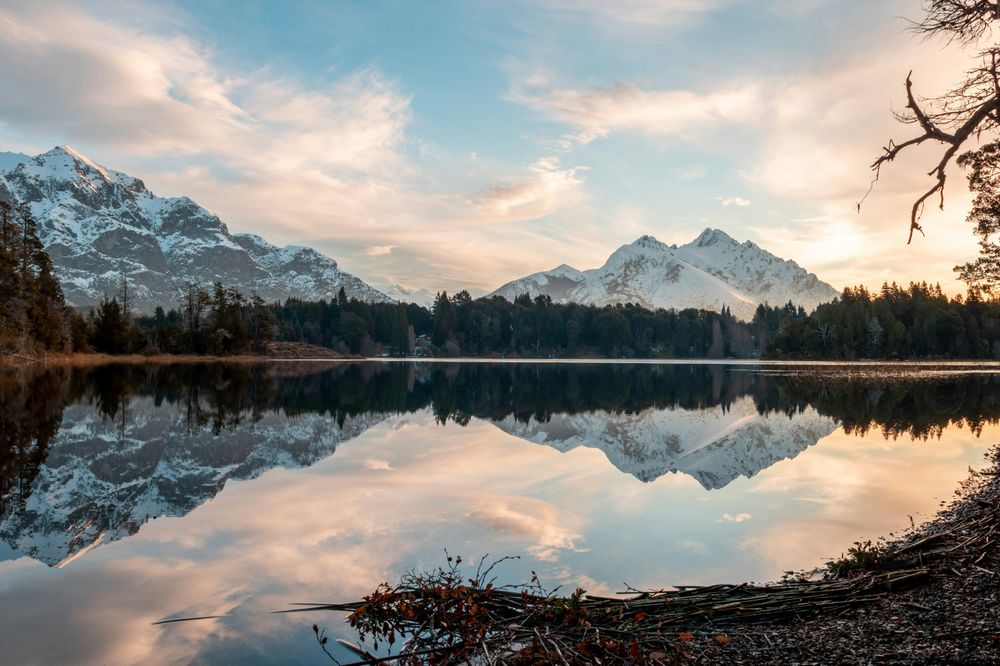 Snow-capped mountains reflected in a pristine alpine lake surrounded by dense forests at sunrise in Patagonia.
