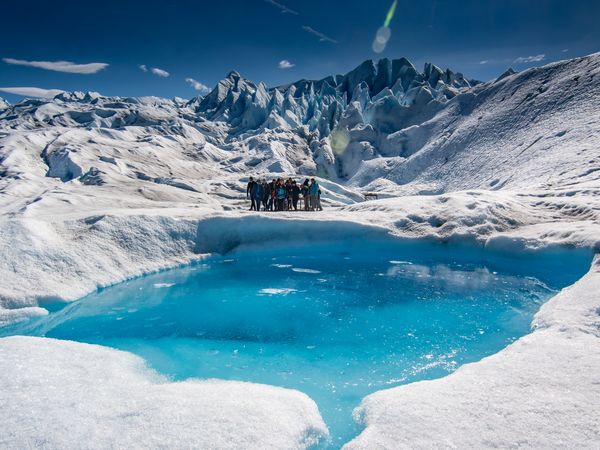 Group of trekkers stand beside a stunning turquoise glacial meltwater pool surrounded by white ice formations in Patagonia.