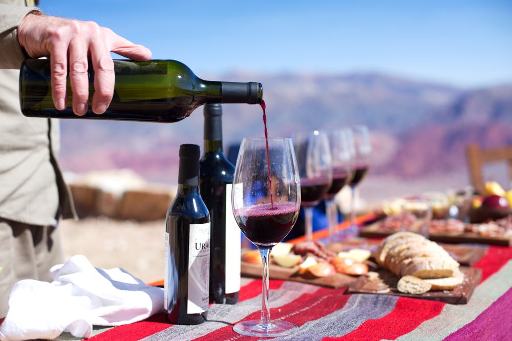 Red wine pouring at a hilltop vineyard picnic in Cafayate with mountain views and traditional Argentine food.