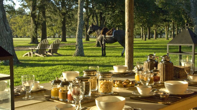 Outdoor dining setup at La Bamba de Areco estancia near Buenos Aires with formal table settings overlooking manicured grounds and horseman.