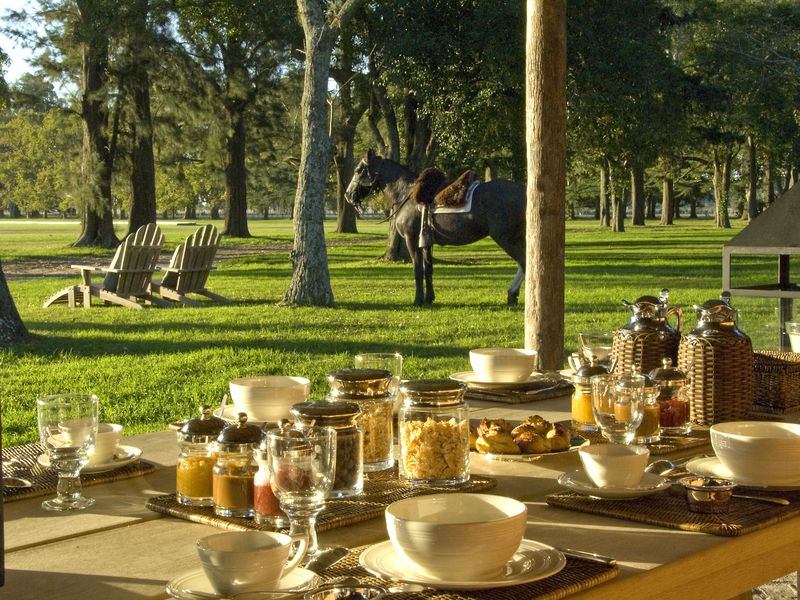 Outdoor dining setup at La Bamba de Areco estancia near Buenos Aires with formal table settings overlooking manicured grounds and horseman.
