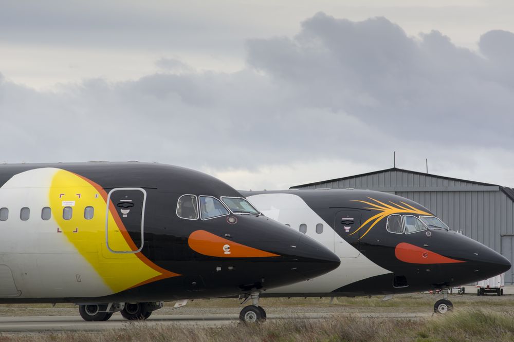 Two commercial aircraft with yellow and orange livery parked at an airport hangar under cloudy skies.