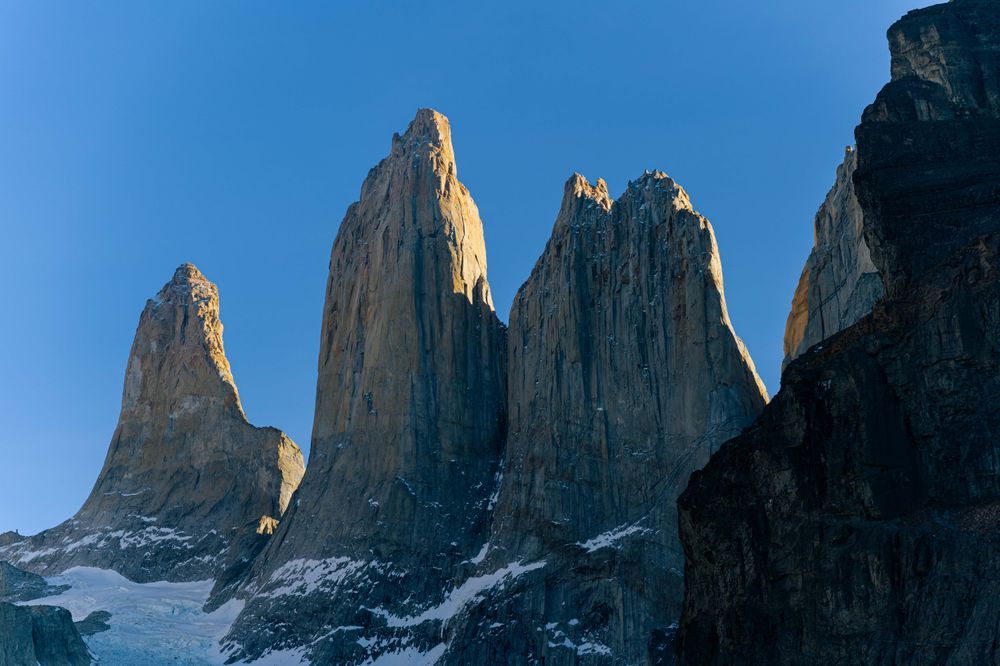 Towering granite peaks of Torres del Paine rise dramatically against clear blue sky in Patagonia, Chile.