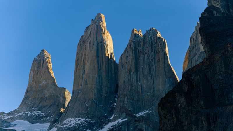 Towering granite peaks of Torres del Paine rise dramatically against clear blue sky in Patagonia, Chile.