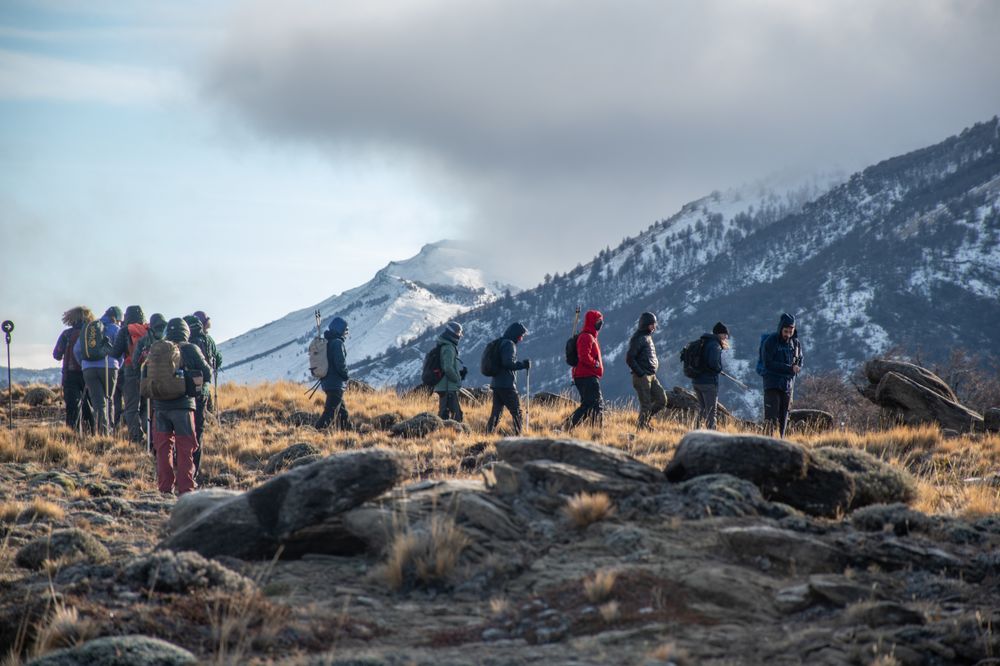 Group of hikers trekking across windswept terrain with snow-capped peaks in Torres del Paine National Park, Patagonia.