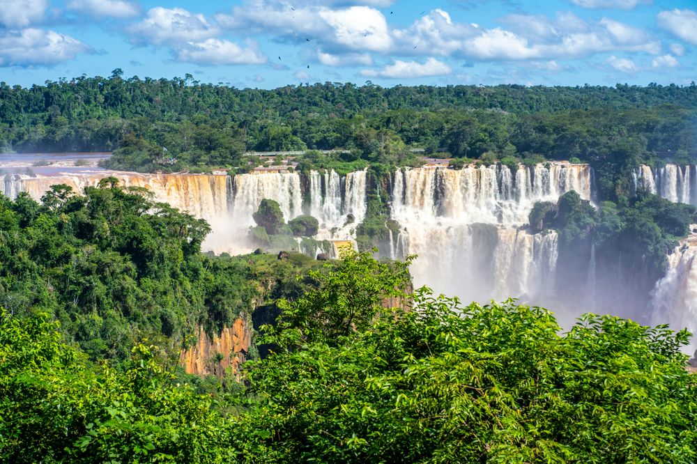 Iguazú Falls cascades through lush rainforest under blue skies in Argentina.