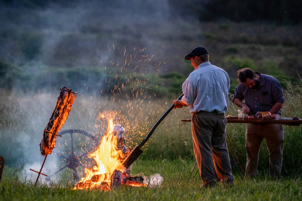 Men gather around a blazing campfire at dusk in the rolling grasslands near Tandil, Buenos Aires.