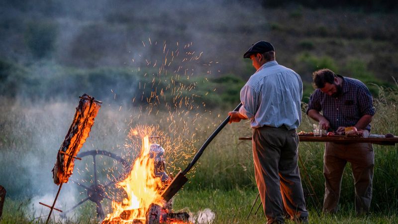 Men gather around a blazing campfire at dusk in the rolling grasslands near Tandil, Buenos Aires.