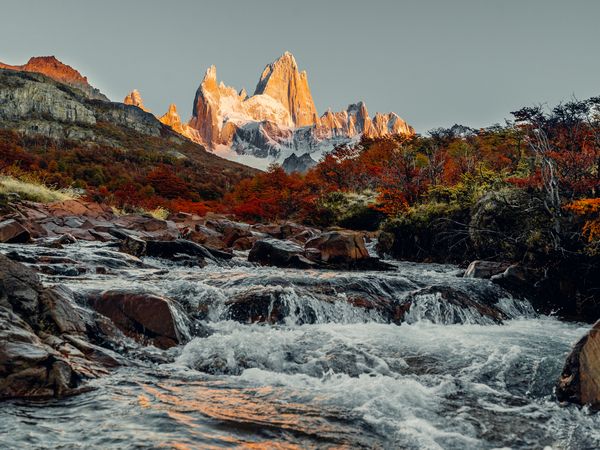 Turquoise river flows past golden granite peaks of Mount Fitz Roy at sunrise in El Chaltén, Patagonia.