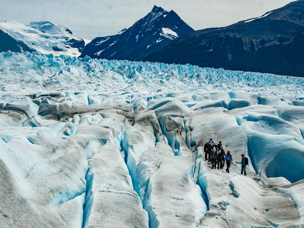 Trekkers explore the turquoise crevasses of Perito Moreno Glacier beneath snow-capped Patagonian peaks.