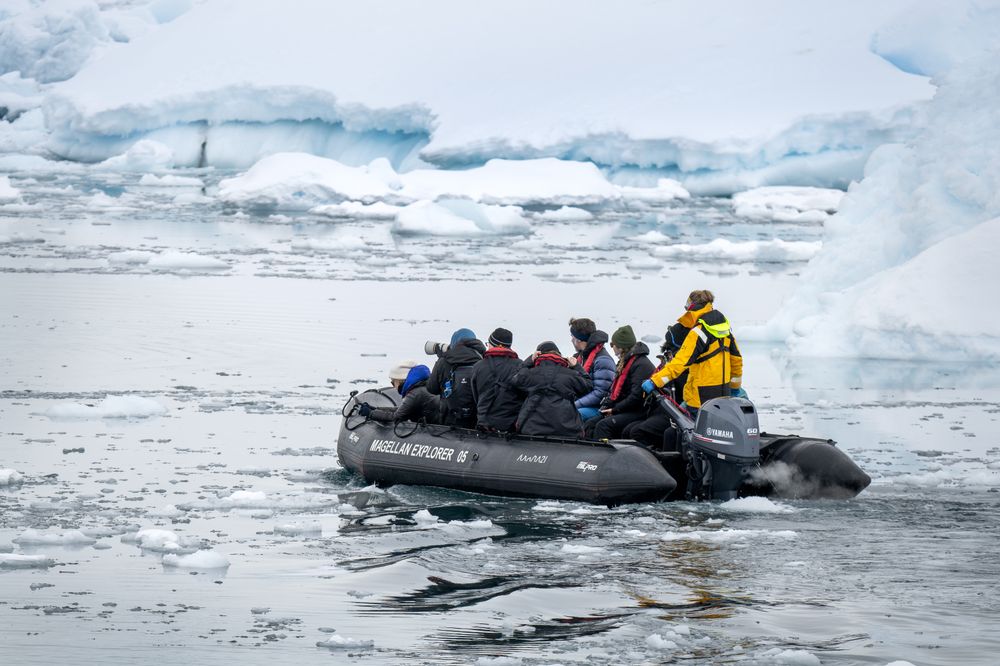 Zodiac boat with tourists navigating through icebergs in Antarctic waters surrounded by glacial ice.