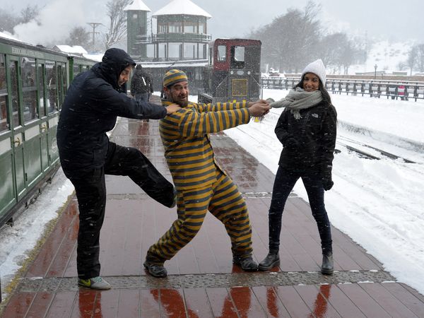 Three friends playfully pose on the platform of Tren Fin del Mundo during a snowy day in Ushuaia, Argentina.