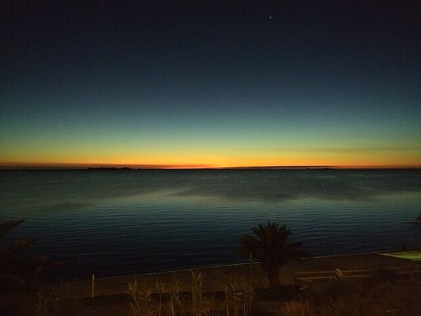 Sunset over the Río de la Plata in Colonia del Sacramento, Uruguay, with palm trees silhouetted on the sandy beach.