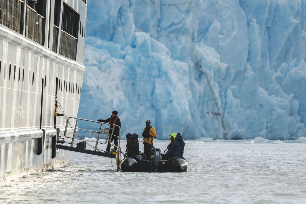 Zodiac boat tour passengers approach a massive blue glacier wall in Antarctica during an expedition cruise.