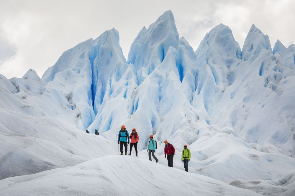Group of hikers in colorful gear exploring towering blue ice formations on Perito Moreno Glacier in Patagonia.