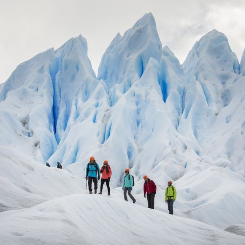 Group of hikers in colorful gear exploring towering blue ice formations on Perito Moreno Glacier in Patagonia.