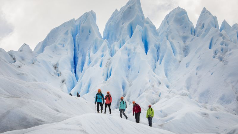Group of hikers in colorful gear exploring towering blue ice formations on Perito Moreno Glacier in Patagonia.