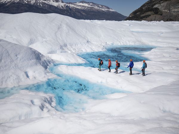 Guided trekkers in colorful jackets explore the blue ice formations and white expanse of Perito Moreno Glacier in Patagonia.