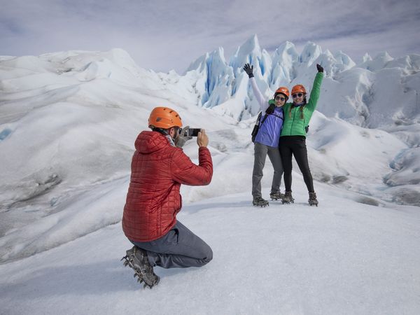 Hikers in safety gear celebrate on Perito Moreno Glacier in El Calafate, surrounded by towering blue ice formations.