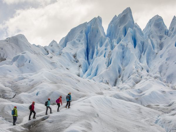 Group of hikers trekking across the pristine blue ice formations of Perito Moreno Glacier in Patagonia, Argentina.