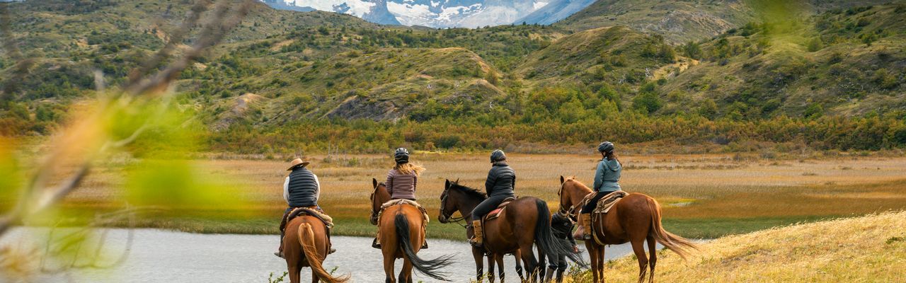 Four horseback riders explore the Patagonian landscape near Torres del Paine with snow-capped peaks behind