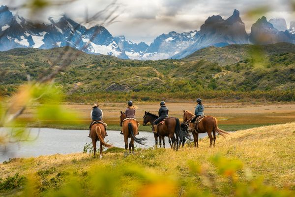 Four horseback riders explore the Patagonian landscape near Torres del Paine with snow-capped peaks behind