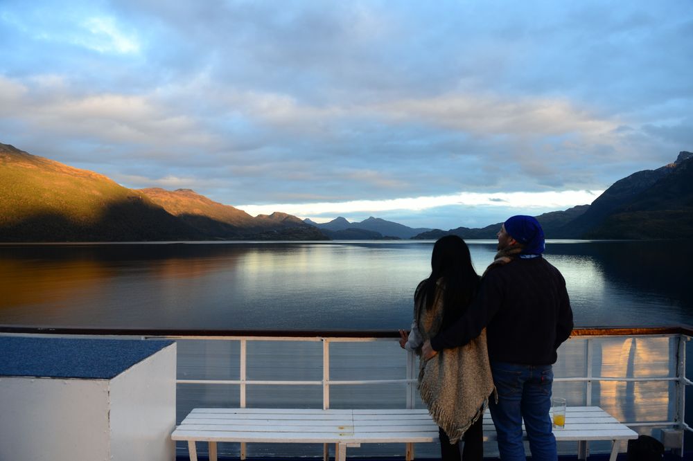 Two travelers admire snow-capped mountains and pristine fjords from a cruise ship deck in Patagonia's Kawéskar Route.