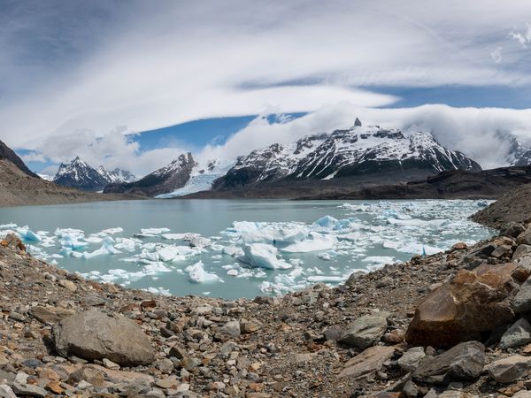 Turquoise glacial lake with icebergs surrounded by snow-capped peaks and rocky moraine in Patagonia's stunning landscape.