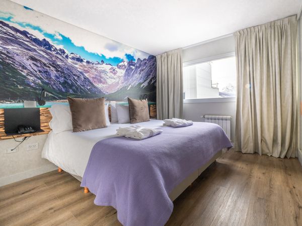 Modern hotel bedroom with mountain and turquoise lake mural overlooking Tierra del Fuego's dramatic Patagonian landscape.