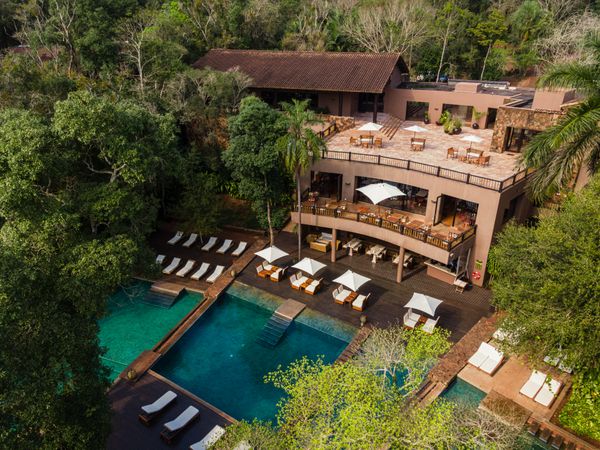 Luxury resort with turquoise pool surrounded by lounge chairs, multi-level terrace, and native forest in Patagonia.