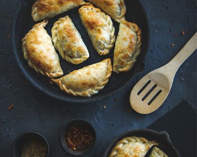 Golden-baked empanadas served in cast iron skillets with traditional spices on a dark surface.