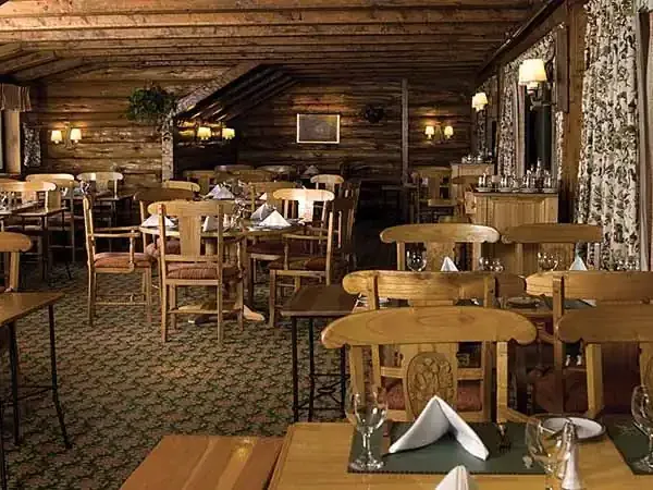 Elegant dining room at Llao Llao Hotel with wooden furnishings, white napkins, and rustic log cabin architecture overlooking Patagonia.