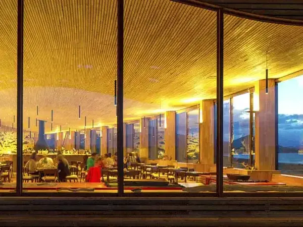 Tierra Patagonia luxury lodge glows warmly at dusk with floor-to-ceiling windows overlooking Patagonian landscape and lake.