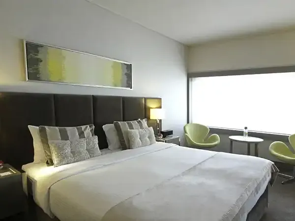 Modern hotel bedroom in Recoleta with minimalist design, white bedding, black headboard, and green accent chairs.