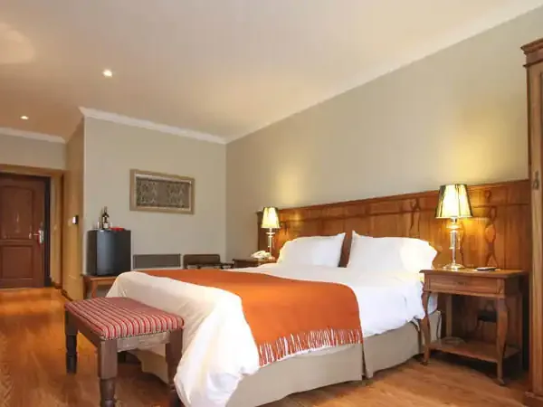 Luxurious hotel bedroom at Chalten Suites featuring wooden furnishings, orange accents, and elegant bedside lighting.