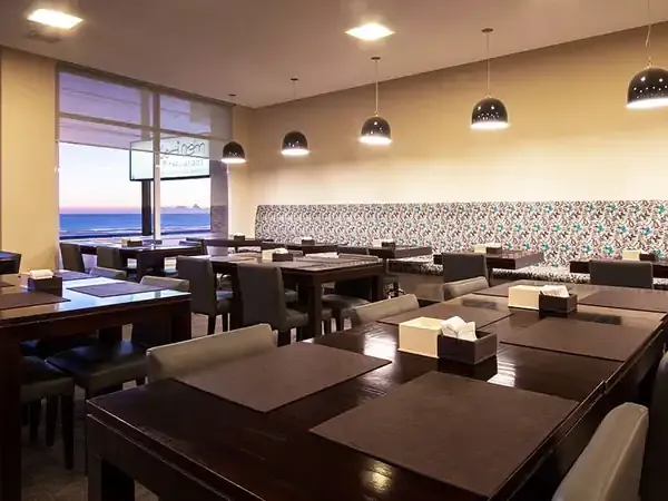 Modern upscale restaurant with ocean views, dark wood tables, pendant lighting, and patterned accent wall in Puerto Madryn.