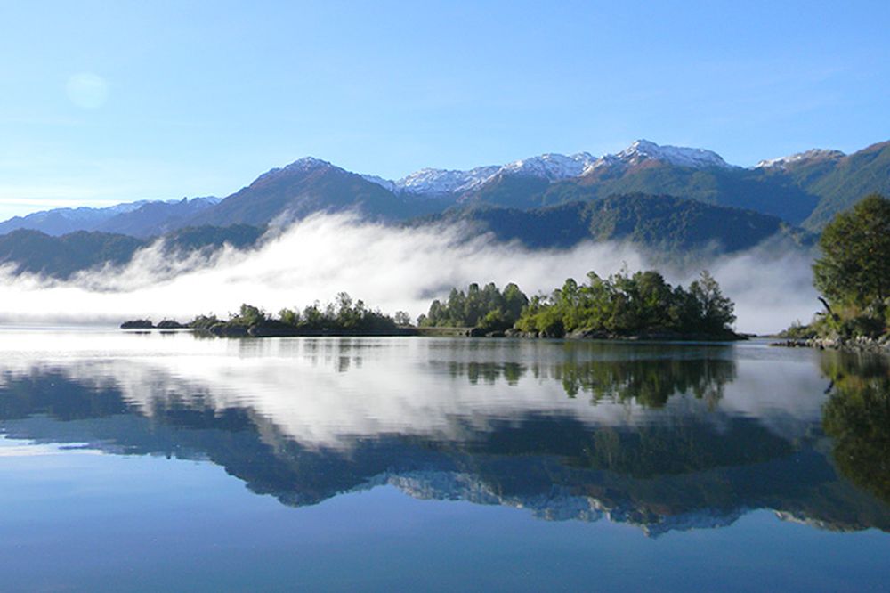Misty mountains reflect in calm waters of Fiordo Puyuhuapi along Chile's Carretera Austral.