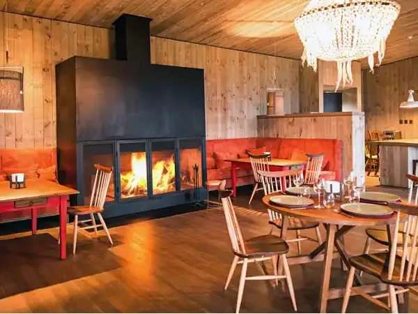 Warm wooden lodge interior at Awasi with active fireplace, dining tables, and red accent seating in Patagonia.