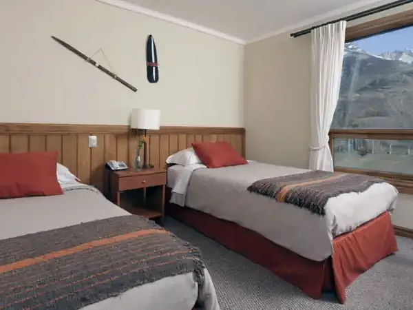 Modern hotel room at Hotel Las Torres with twin beds, red accents, and panoramic mountain views of Patagonia.