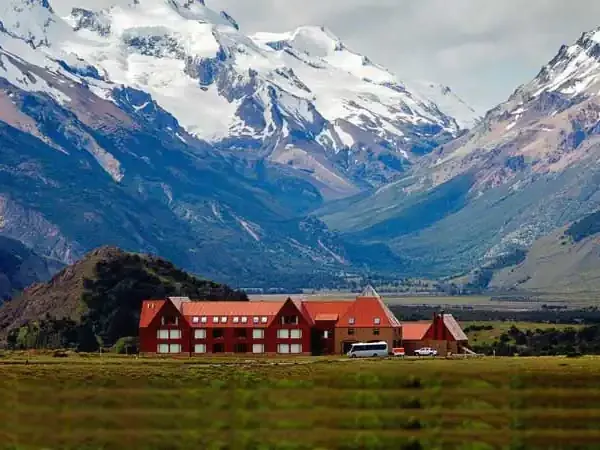 Red-roofed Los Cerros Boutique Hotel nestled in a lush valley beneath snow-capped Patagonian mountains.