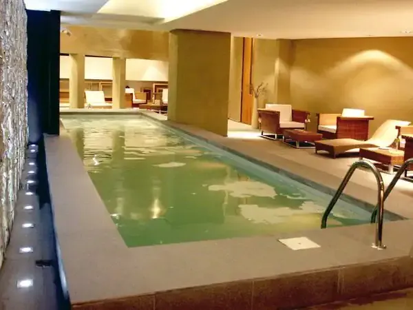 Luxury indoor swimming pool with green water, modern lounge chairs, and warm ambient lighting at Hotel Esplendor.