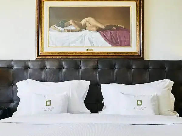 Luxury bedroom at El Casco hotel in Patagonia with elegant black headboard, white linens, and classical artwork above.