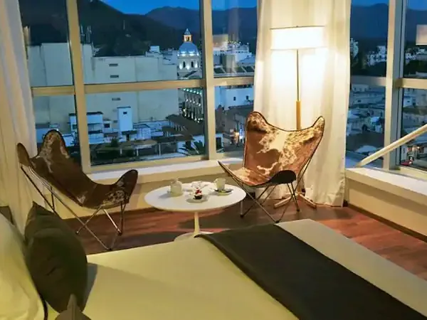 Modern hotel suite in Bariloche with panoramic Andean views, butterfly chairs, and elegant evening ambiance.