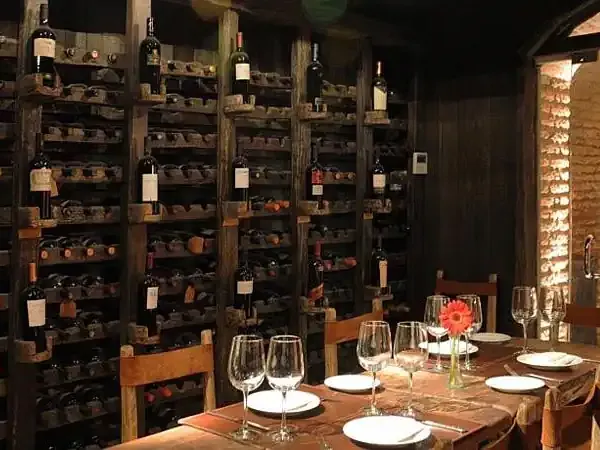 Wine cellar dining room with set table and extensive bottle collection on wooden shelves.