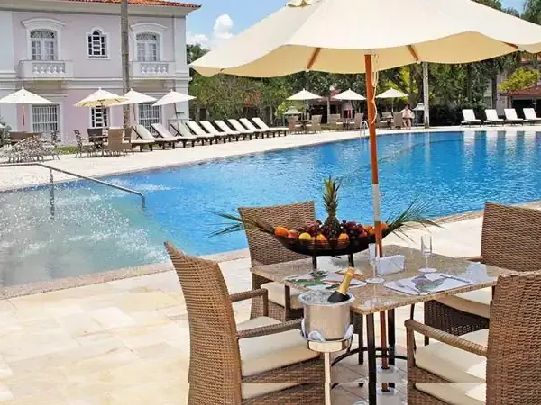 Luxurious poolside dining at Belmond resort with elegant wicker seating, yellow umbrellas, and a sparkling blue swimming pool.